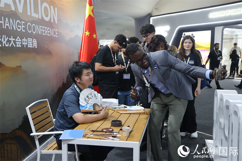 “中国角”外围，参观者与在折扇上进行书法创作的工作人员合影。人民网记者  时元皓摄